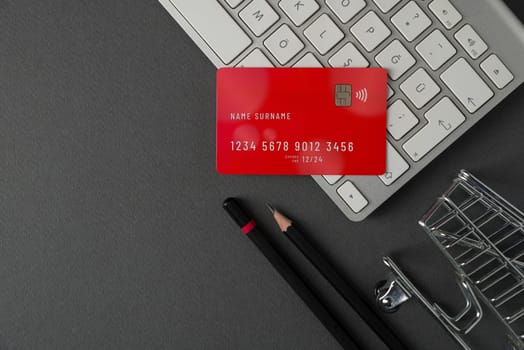 Top view of computer keyboard, credit card and mini market cart on dark gray table