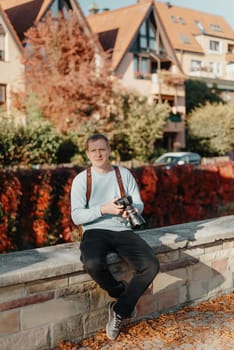 Man Sitting on Stairs in Old European City And Holding Photo Camera. Contemporary Stylish Blogger And Photographer