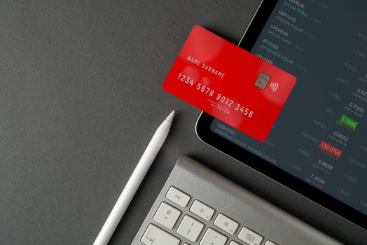 Top view of tablet with live exchange rates on screen, red credit card and keyboard on black table