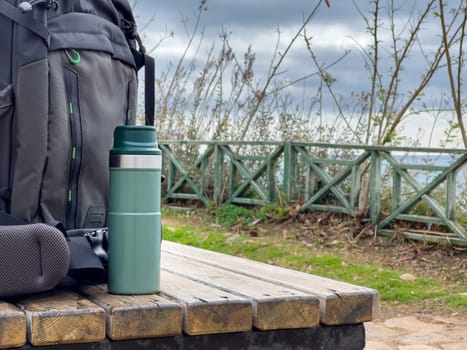 Backpack and thermos standing on wooden table in nature park