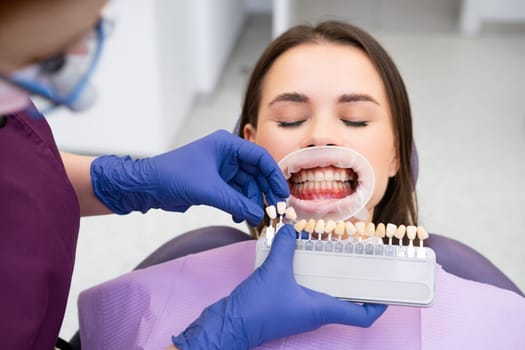 Dentist selects a shade of teeth whitening for young woman with perfect smile.