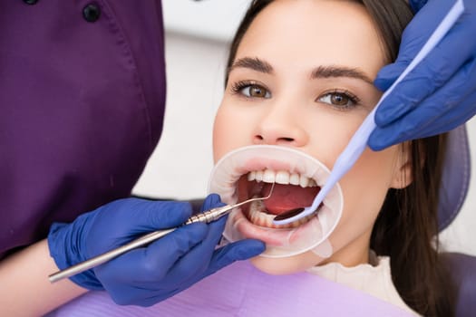 Woman patient undergoes dental treatment in clinic. Female dentist in gloves meticulously checks strength of teeth using specialized instruments