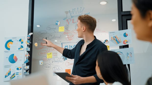 Professional male leader presents start up project by using mind map, colorful sticky notes and business statistic graph with confident while investor listening carefully. Immaculate.