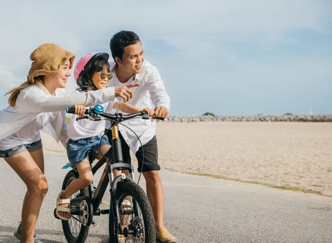 On sandy beach near sea cheerful family enjoys summer road trip teaching and learning bicycle riding. Parents guide their children creating joyful and memorable vacation moment.