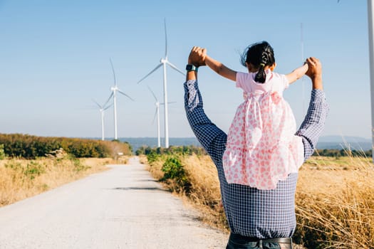Dad carries daughter at wind farm exploring future. Family bonding by turbines signifies innovation in renewable energy. A joyful father-daughter moment in the windmill industry. father day concept
