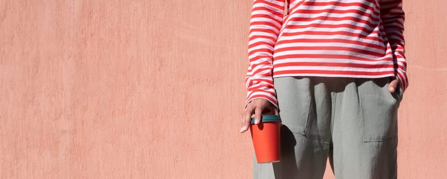 Woman in striped shirt holding red cup and drinking coffee. Close up hand with paper cup.