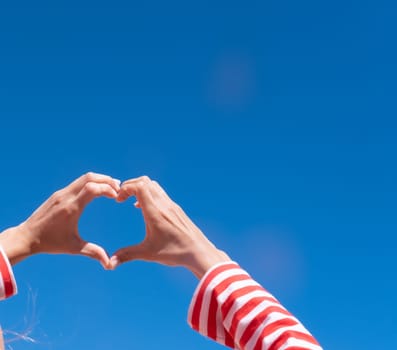 Female hands making sign Heart by fingers on sky background. Beautiful hands of woman with copy space. Love concept on Valentine day.