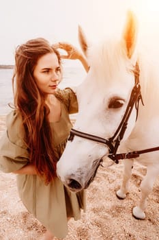 A woman in a dress stands next to a white horse on a beach, with the blue sky and sea in the background