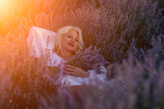 Blonde woman poses in lavender field at sunset. Happy woman in white dress holds lavender bouquet. Aromatherapy concept, lavender oil, photo session in lavender.