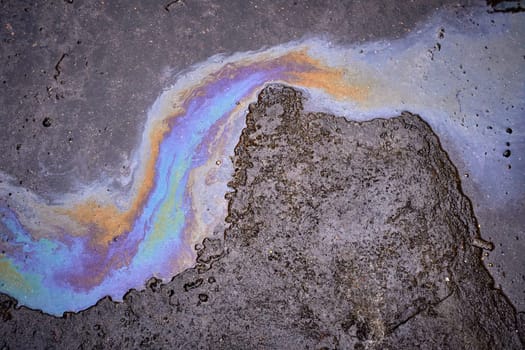 Leakage of oil or gasoline from under the car on the asphalt in the parking lot.