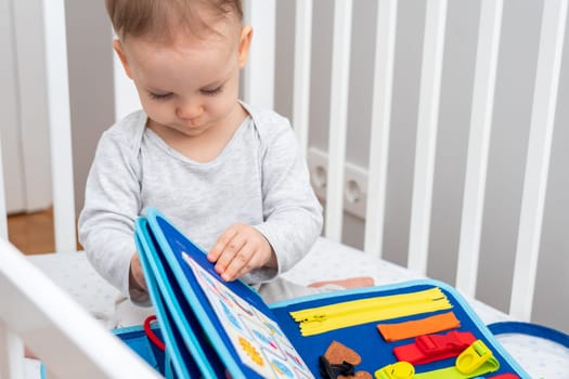 Baby girl playing with montessori busy book sitting in a crib