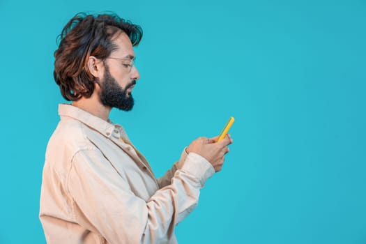 A man with facial hair is making a speech using hand gestures while holding a cell phone on an azure background