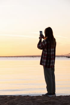 silhouette of woman taking a mobile picture of sunrise on the beach