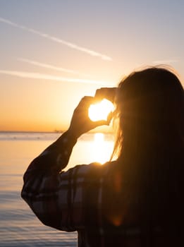 hands forming a heart shape with sunset silhouette on the beach