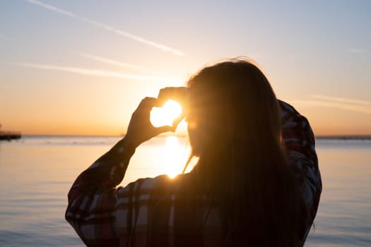 hands forming a heart shape with sunset silhouette on the beach