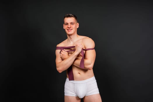 Young bodybuilder working out with rubber band over a white and dark background