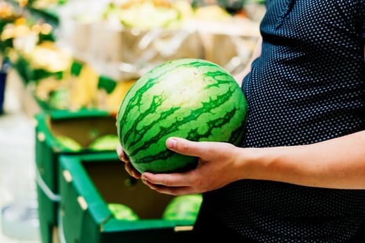 Hand is holding watermelon from the supermarket shelf, close up photo