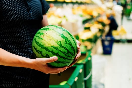 Hand is holding watermelon from the supermarket shelf, close up photo