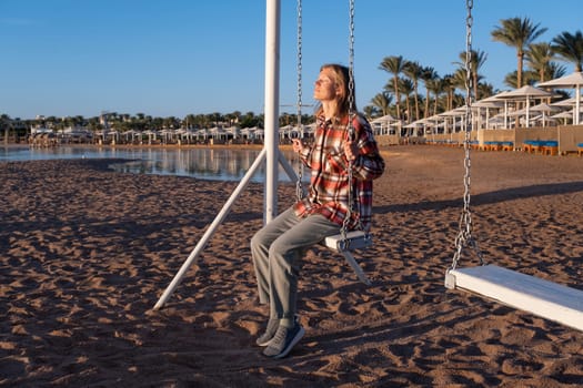 beautiful young woman on the swing on the beach in sunrise and sky background