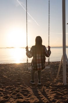 beautiful young woman on the swing on the beach in sunrise and sky background, back view