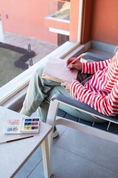 Draw in sketchbook. back view of a woman sketching in sketchbook sitting on the balcony