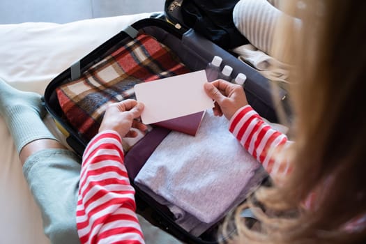 happy woman preparing for holidays, packing suitcase on bed, woman holding a blank boarding pass