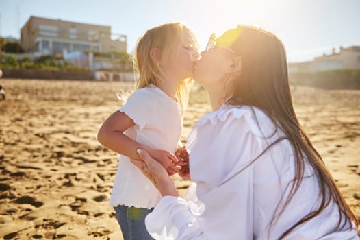 Happy loving mother kissing her adorable daughter on the beach