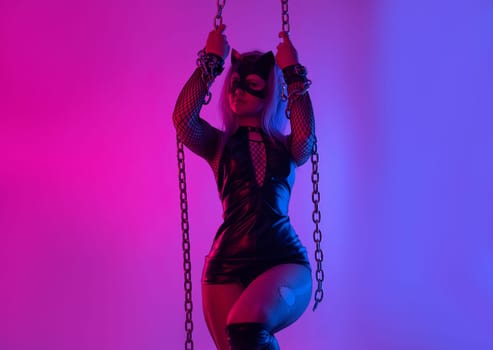 Sexy girl in latex BDSM mistress dress and cat mask in neon light on dark background with chains sex game
