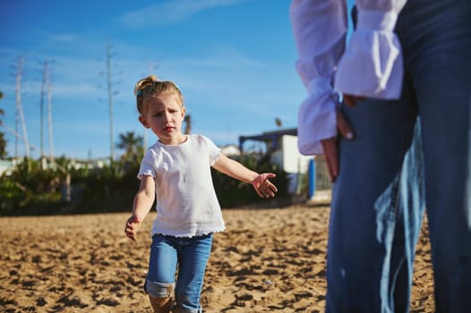 Close-up lifestyle portrait of a mother and daughter walking together on the sandy beach