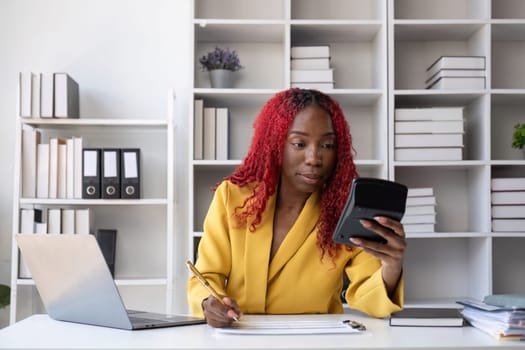 Young African American business woman uses a calculator to calculate numbers. Company financial accounts on desk in office.