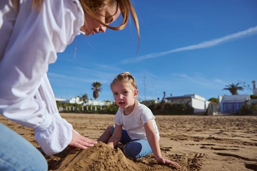 Close up portrait of a Caucasian happy of mother and daughter building castle in sand at beach. Family lifestyle, Leisure activity, People. Vacations