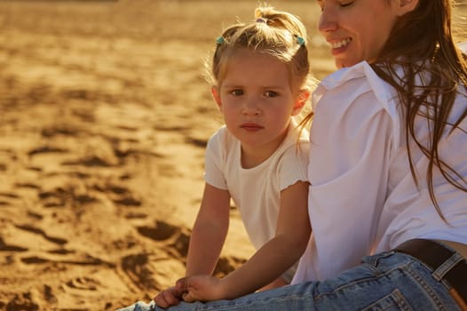 Close-up portrait of a mother and daughter relaxing on the beach together at sunset. People. Active healthy lifestyle