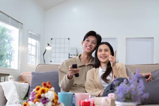 A young Asian couple gives flowers to each other on their anniversary and sits happily together in the living room..