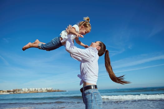 Happy loving caring young mother and her cute daughter playing on the beach together