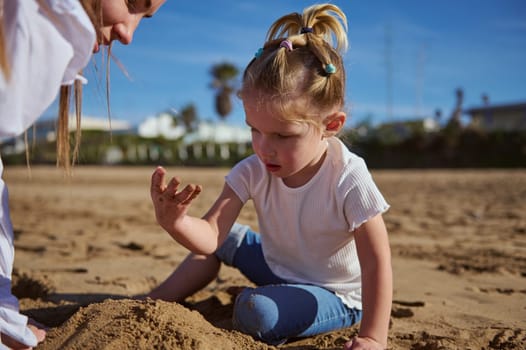 Little girl building sandy castle on the beach. Mother and daughter playing together outdoor