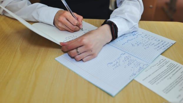 A girl student writes math formulas in a notebook