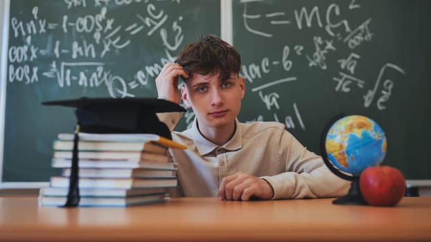 Portrait of a high school student against a background of blackboard, globe and books with cap
