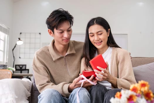 A young Asian couple gives each other gifts on their anniversary and sits happily together in the living room..