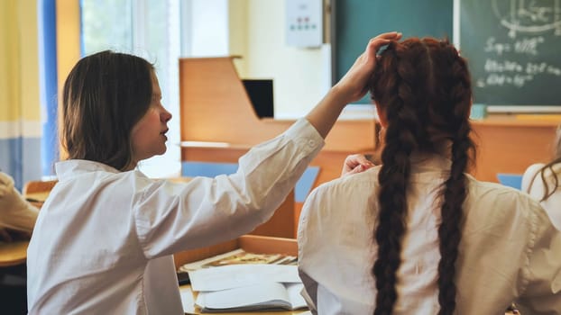 A friend strokes her friend's hair at her desk at school