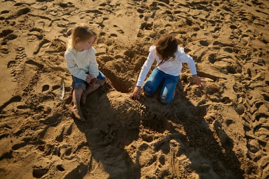 Two adorable little girls, sister sitting on the beach and building a sand castle. Concept of the family vacation. Happy carefree childhood. Overhead view