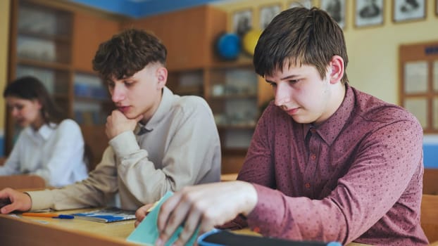 Schoolboys at a desk during class. The boy eats an apple