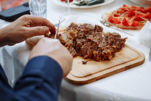 Person in blue suit slicing juicy roasted meat on cutting board surrounded by assorted dishes on table, ready for a delicious meal.