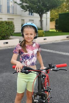 A girl in a helmet holds her red bicycle