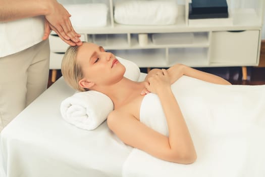 Caucasian woman enjoying relaxing anti-stress head massage and pampering facial beauty skin recreation leisure in dayspa modern light ambient at luxury resort or hotel spa salon. Quiescent