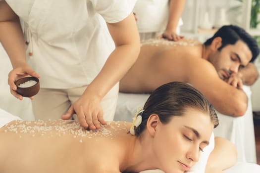 Blissful couple customer having exfoliation treatment in luxury spa salon with warmth candle light ambient. Salt scrub beauty treatment in health spa body scrub. Quiescent