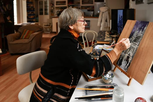 PARIS, FRANCE - FEBRUARY 05, 2021: An elderly woman paints french gothic cathedral at home