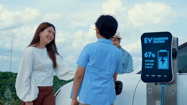 Modern family travel and nature with eco-friendly EV car concept, recharging battery from charging station using renewable energy from wind turbine for future energy sustainability. Peruse