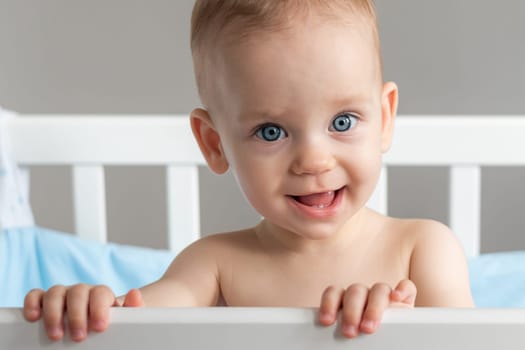 Portrait of one year old baby standing in a crib smiling