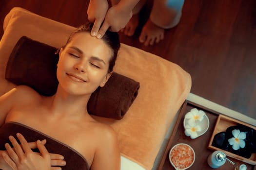 Caucasian woman enjoying relaxing anti-stress head massage and pampering facial beauty skin recreation leisure in warm candle lighting ambient salon spa in luxury resort or hotel. Quiescent