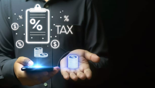 A digital composite image of a person in a dark shirt using a smartphone with a glowing holographic icon of a clipboard labeled 'TAX' above their open palm. Alongside the clipboard are coins and a percentage sign, symbolizing financial obligations related to taxation. The image conveys a concept of tax calculation or financial management, with a dark background and a soft focus on the hand, smartphone, and holographic elements.